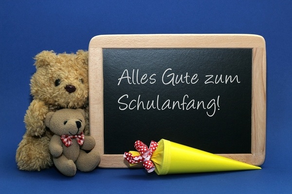 Teddyb&auml;ren und eine schwarze Tafel mit der wei&szlig;en Aufschrift: Alles Gute zum Schulanfang!. Davor liegt eine gelbe Schult&uuml;te.