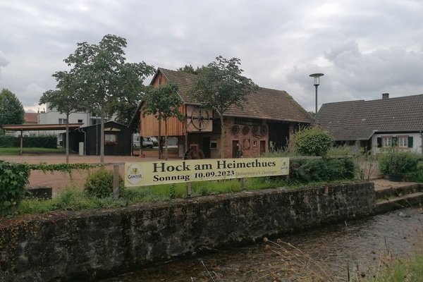 Blick auf den Banner mit der Aufschrift "Hock am Heimethues Sonntag, 10.09.2023", angebracht am Glottergelnder, im Hintergrund die Museumsscheune