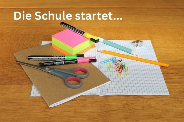 Die Schule startet ... Schulutensilien auf einem Tisch, wei&szlig;e Schrift auf h&ouml;lzernem Untergrund